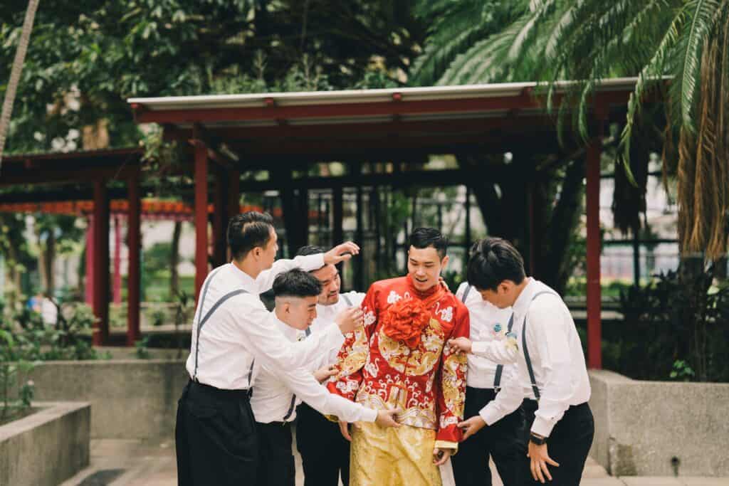 Groom and groomsmen in traditional Chinese attire during a wedding ceremony in Hong Kong garden setting.