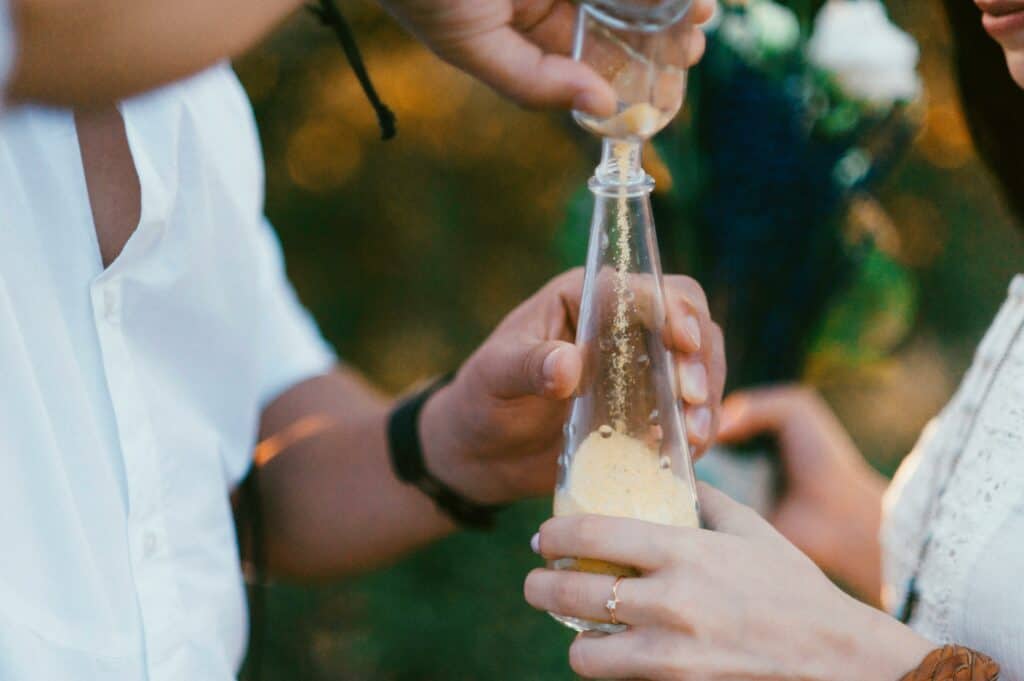 Close-up of two people pouring sand into a glass bottle, symbolizing unity.