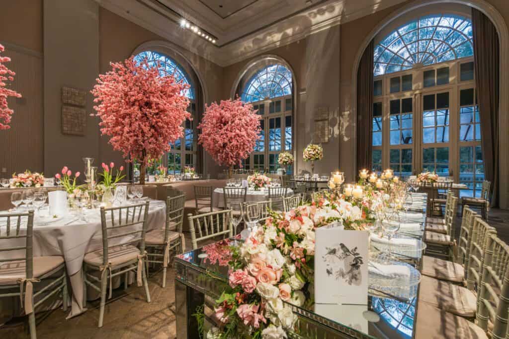 Luxurious wedding reception setup with pink floral arrangements and elegant table settings indoors.